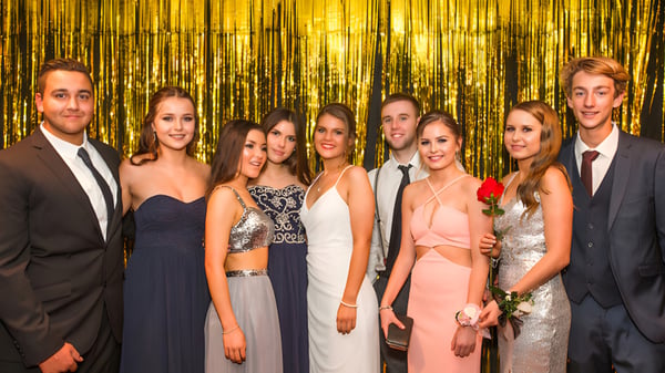 Eine Gruppe von gut gekleideten Schülerinnen und Schülern steht vor einem glänzenden goldenen Hintergrund auf dem Campus der Mercury Bay Area School.