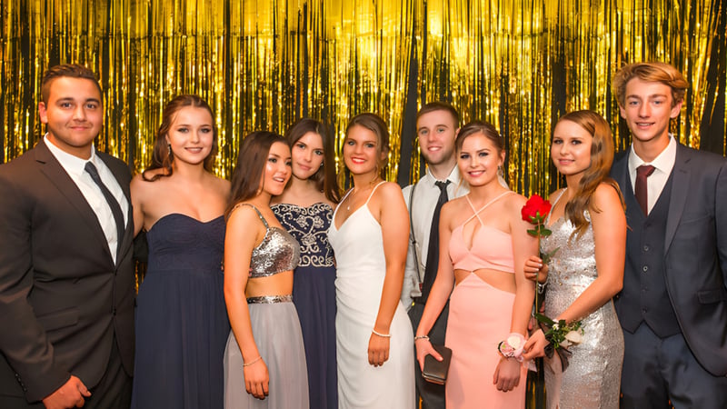 Eine Gruppe von gut gekleideten Schülerinnen und Schülern steht vor einem glänzenden goldenen Hintergrund auf dem Campus der Mercury Bay Area School.