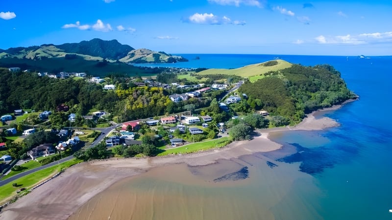 Die Küste mit Sandstrand und grünen Hügeln in der Nähe der Mercury Bay Area School.