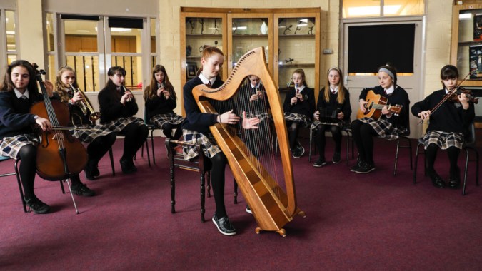 Eine Gruppe Musiker, darunter eine Harfenistin, steht gemeinsam in einem Raum auf dem Campus des Mercy College.