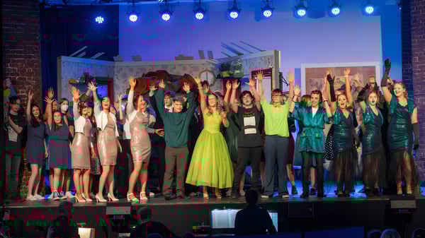 Eine Gruppe von Schülerinnen und Schülern der Mercy Secondary School steht auf einer Bühne mit bunter Beleuchtung vor einem Stadt-Skyline-Hintergrund.