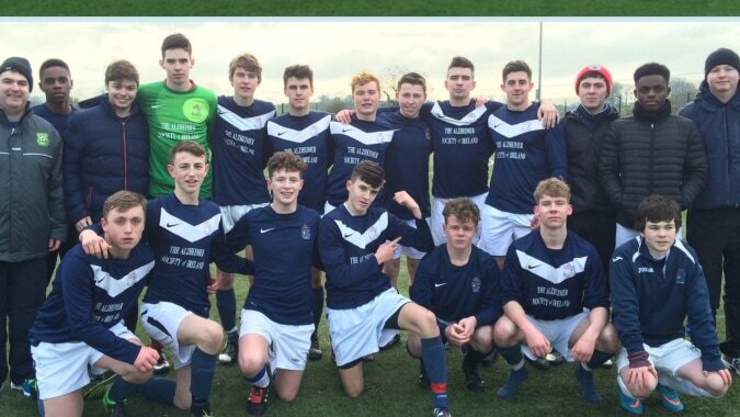 Eine Gruppe männlicher Fußballspieler der Mercy Secondary School steht auf einem Rasenfeld unter bewölktem Himmel.