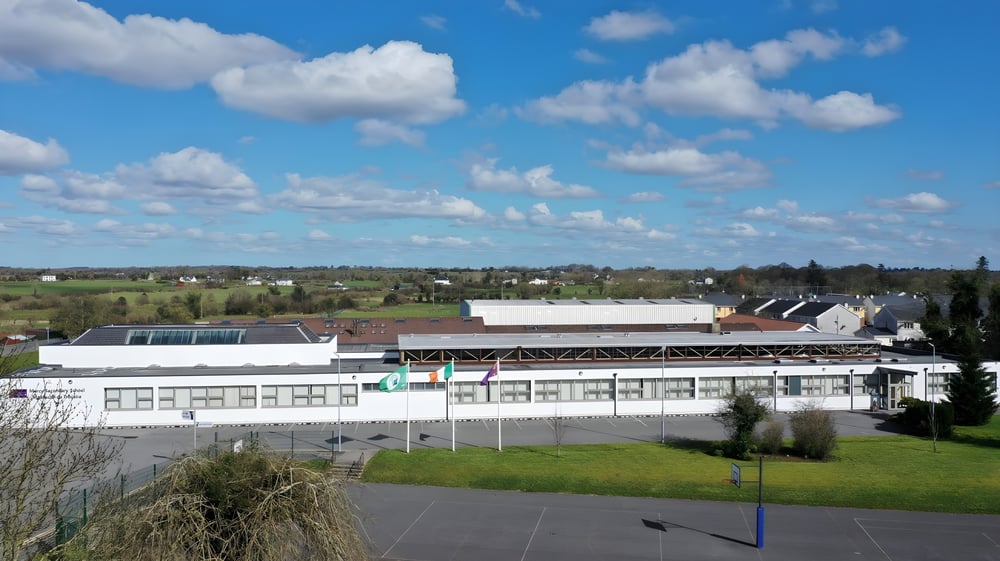 Das Gebäude der Mercy Secondary School steht in einer ländlichen Umgebung mit Grasflächen und bewölktem Himmel im Hintergrund.