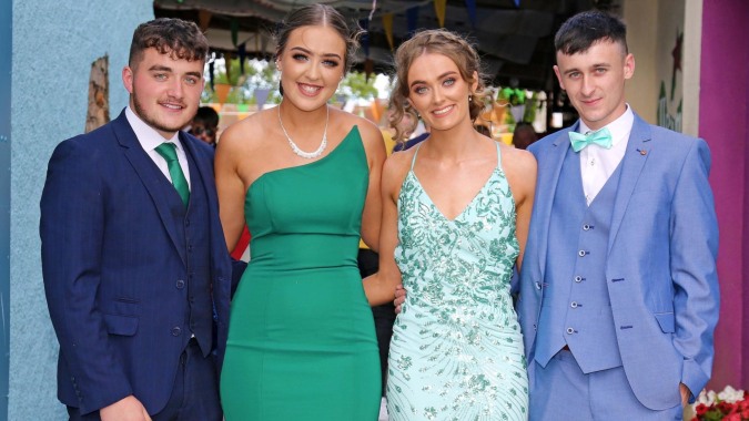 Vier gut gekleidete Personen posieren gemeinsam vor einem farbenfrohen Hintergrund auf der Mercy Secondary School.