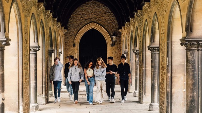 Eine Gruppe Schülerinnen und Schüler geht durch den mit Säulen und Bögen verzierten Hofgang der Mercy Secondary School.