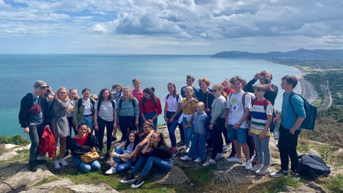 Schüler der Mercy Secondary School stehen auf einer Klippe und blicken auf eine Küstenlandschaft mit Wasser und Bergen.