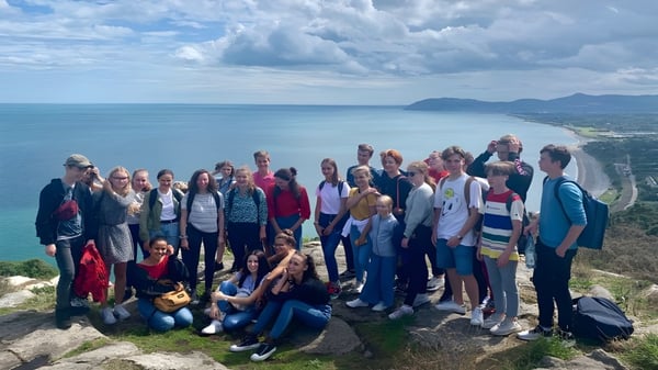 Schüler der Mercy Secondary School stehen auf einem Felsen und blicken auf die Küstenlandschaft mit Wasser und Bergen.