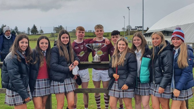 Eine Gruppe Schülerinnen und Schüler der Mercy Secondary School posiert gemeinsam mit einem Pokal auf dem Sportfeld der Schule.