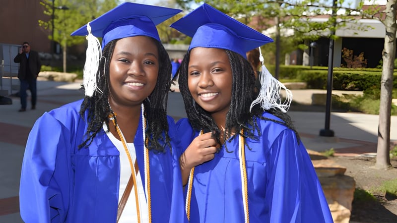 Zwei Schülerinnen in blauen Abschlussroben stehen zusammen vor einem Campusgebäude des Meridan State College.