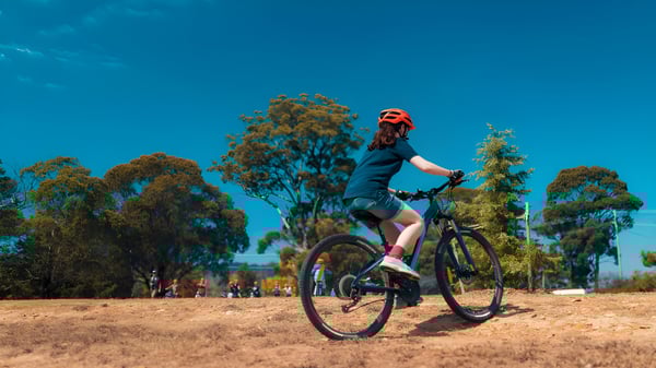 Eine Schülerin des Meridan State College fährt mit einem Mountainbike auf einem Waldweg unter blauem Himmel.
