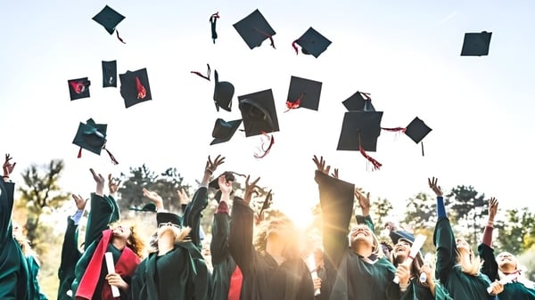 Absolventen der Merivale High School werfen ihre Abschlussmützen in die Luft vor Bäumen und untergehender Sonne.