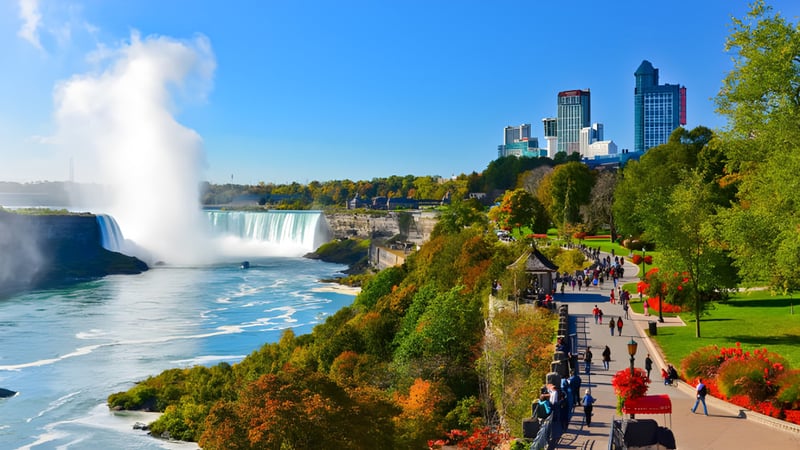 Ein Wasserfall fließt in einen Fluss vor der Kulisse von Grünflächen und Hochhäusern in der Nähe der Merivale High School.