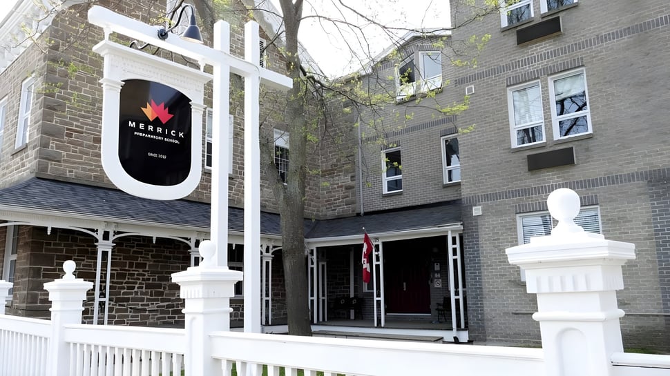 Das steinerne Gebäude mit weißem Eingangsbereich der Merrick Preparatory School ist von Bäumen umgeben.