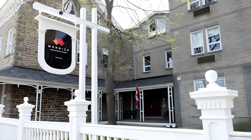 Das steinerne Gebäude mit weißem Eingangsbereich der Merrick Preparatory School ist von Bäumen umgeben.