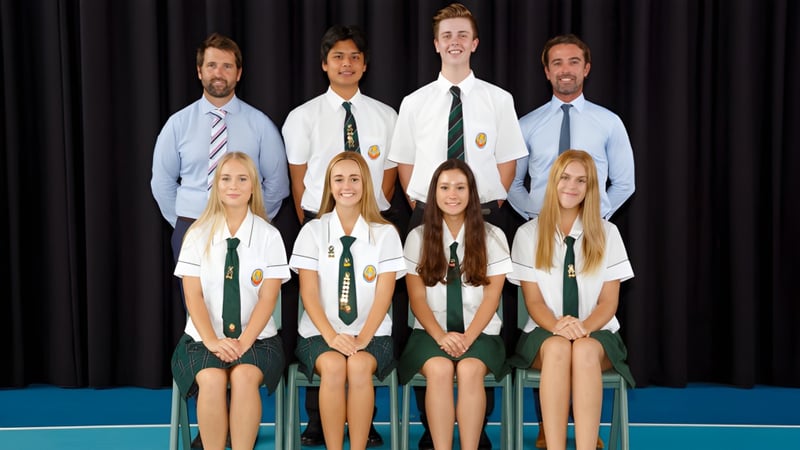 Eine Gruppe von Schülerinnen und Schülern der Merrimac State High School sitzt in Schuluniformen vor dunklem Hintergrund in formaler Pose.