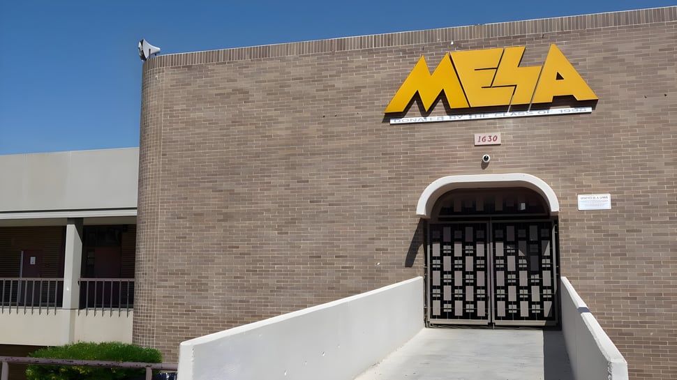 Das Backsteingebäude mit einem gelben MESA-Schild zeigt die Fassade der Mesa High School bei klarem Himmel.