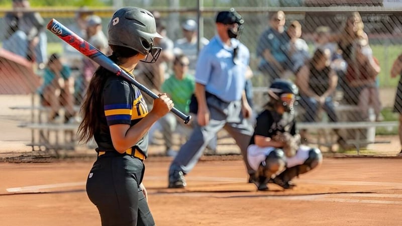 Eine Softballspielerin steht auf dem Spielfeld des Mesa Unified School District mit anderen Spielern und Zuschauern im Hintergrund.