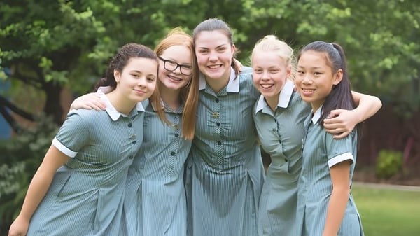 Eine Gruppe von Schülerinnen des Methodist Ladies' College steht in grünen Schuluniformen gemeinsam in einem grünen Außenbereich.