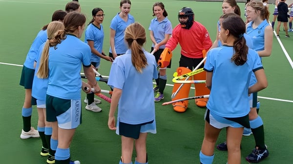 Eine Gruppe junger Sportlerinnen in blauen Trikots steht auf dem Sportplatz des Methodist Ladies' College um eine Spielerin in rotem Trikot.
