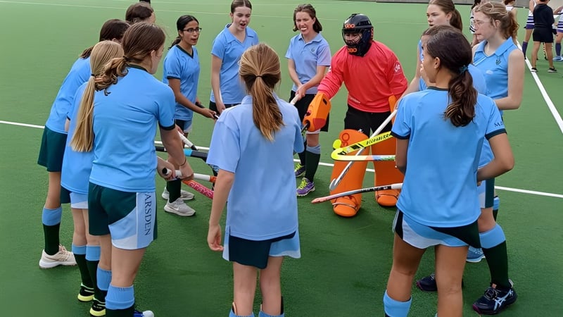 Eine Gruppe junger Sportlerinnen in blauen Trikots steht auf dem Sportplatz des Methodist Ladies' College um eine Spielerin in rotem Trikot.