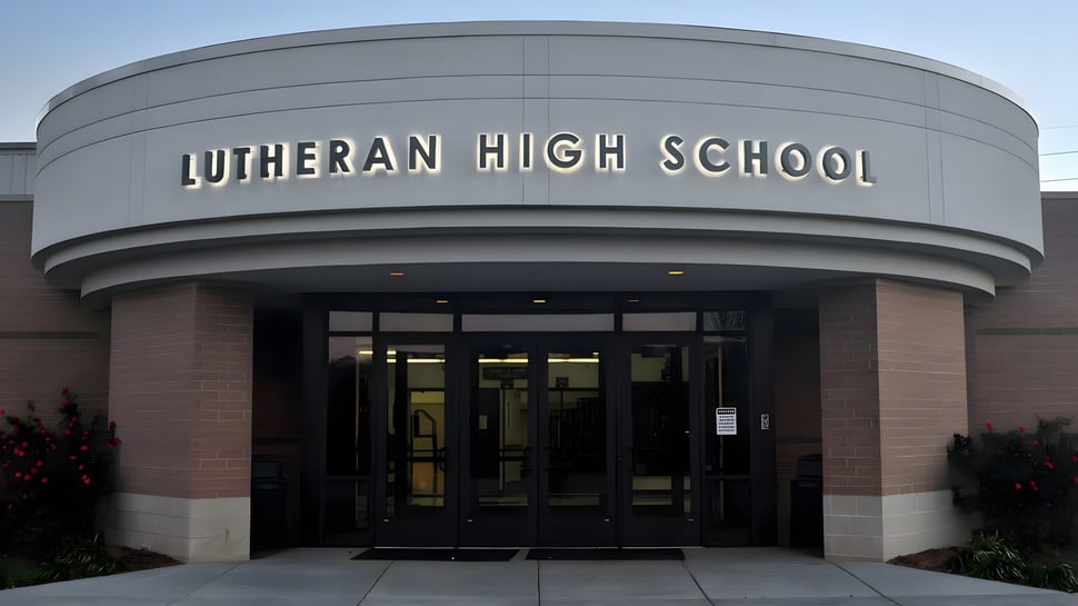 Der Eingang der Metro East Lutheran High School zeigt ein großes modernes Gebäude mit einem gewölbten Dach und einem auffälligen Schild über dem Eingang.