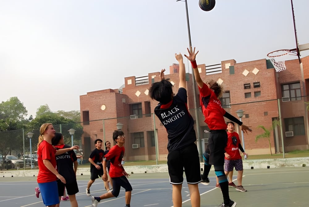 Schüler der Metro International Secondary Academy spielen Basketball auf einem Außenplatz vor Backsteingebäuden.