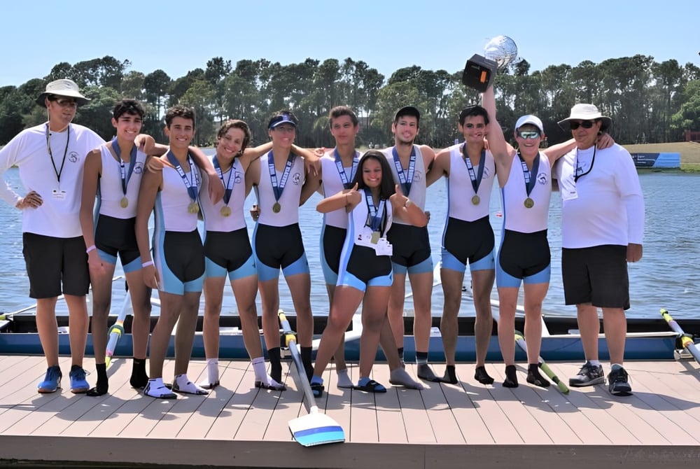 Eine Gruppe von Schülerinnen und Schülern der Miami Beach Senior High School steht als Ruderteam gemeinsam auf einem Steg am Wasser.
