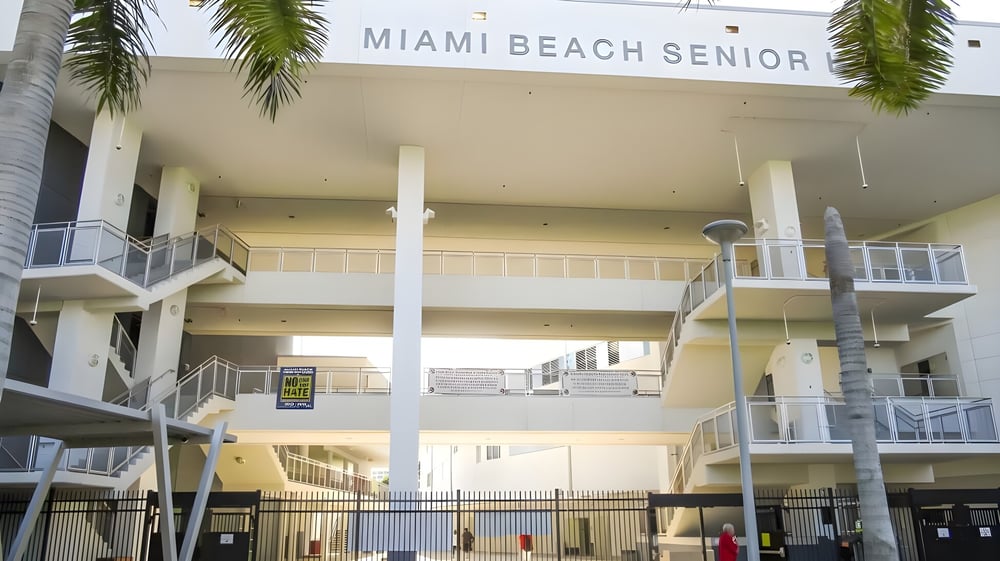 Das mehrstöckige Gebäude der Miami Beach Senior High School ist von Palmen umgeben und durch einen Zaun abgegrenzt.