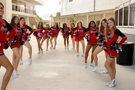 Eine Gruppe von Cheerleaderinnen in roten und schwarzen Uniformen mit Pompons steht auf dem Campus der Miami-Dade County Public School.