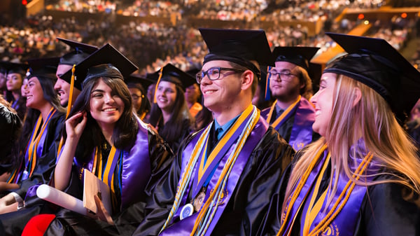 Absolventinnen und Absolventen in bunten Abschlussroben stehen bei der Abschlussfeier der Miami State High School zusammen.