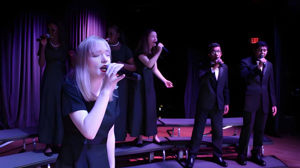 Eine Frau in weißem Kleid singt auf der Bühne bei einer Aufführung der Miami Arts Charter School.