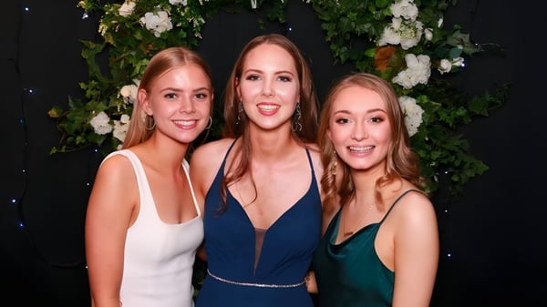 Drei Schülerinnen der Middleton Grange School in formeller Kleidung stehen vor einem Blumenhintergrund.