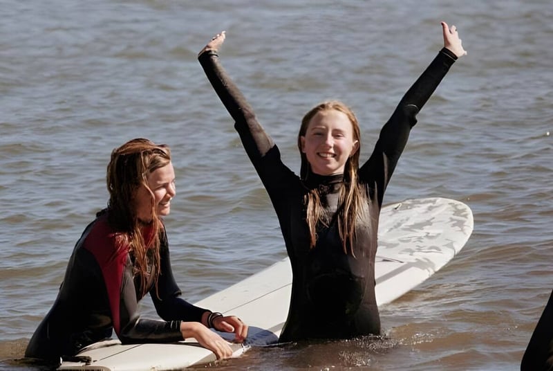 Zwei Personen in Neoprenanzügen stehen im flachen Wasser und feiern auf dem Gelände der Midland School.
