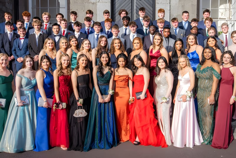 Eine Gruppe von Schülerinnen und Schülern des Midleton College steht in formeller Kleidung vor einem Steingebäude.