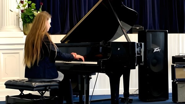 Eine Frau mit langen blonden Haaren spielt Klavier auf der Bühne des Midleton College vor einem schwarzen Vorhang.