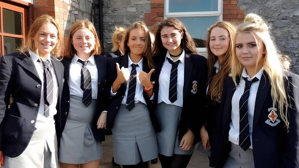Eine Gruppe von sechs Schülerinnen in Schuluniformen steht vor einem Backsteingebäude auf dem Campus des Midleton College.