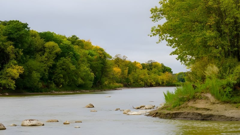 Ein ruhiger Fluss fließt durch eine herbstliche Landschaft mit bunten Bäumen an der Miles Macdonell Collegiate.