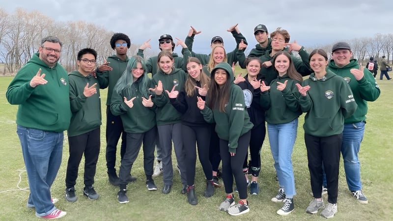 Eine Gruppe von Schülern der Miles Macdonell Collegiate steht mit grünen Kapuzenpullovern auf einem Feld im Freien.