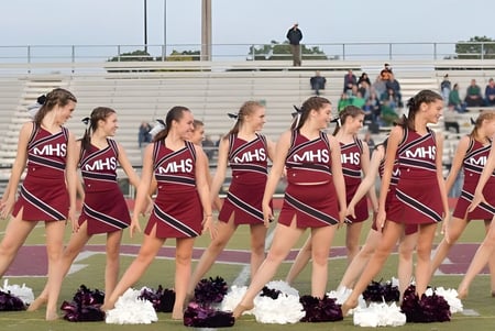 Eine Gruppe Cheerleader in passenden Uniformen steht auf dem Sportfeld des Milford Public School Districts vor Zuschauern.
