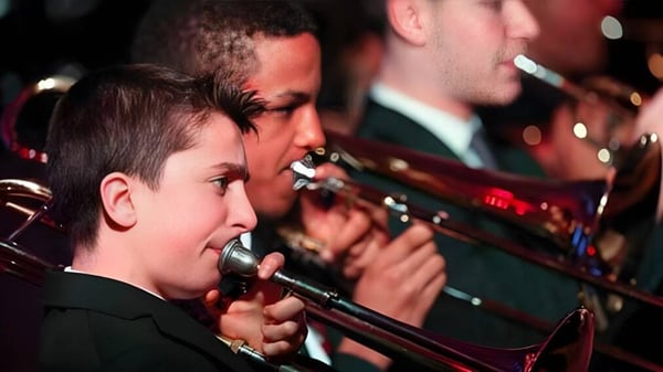Ein Junge singt in einem Konzert auf der Bühne der Mill Hill International School mit Band im Hintergrund.