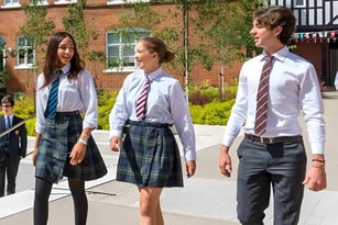 Drei Schülerinnen und Schüler der Mill Hill International stehen vor einem ziegelgedeckten Gebäude mit efeubewachsenen Wänden.