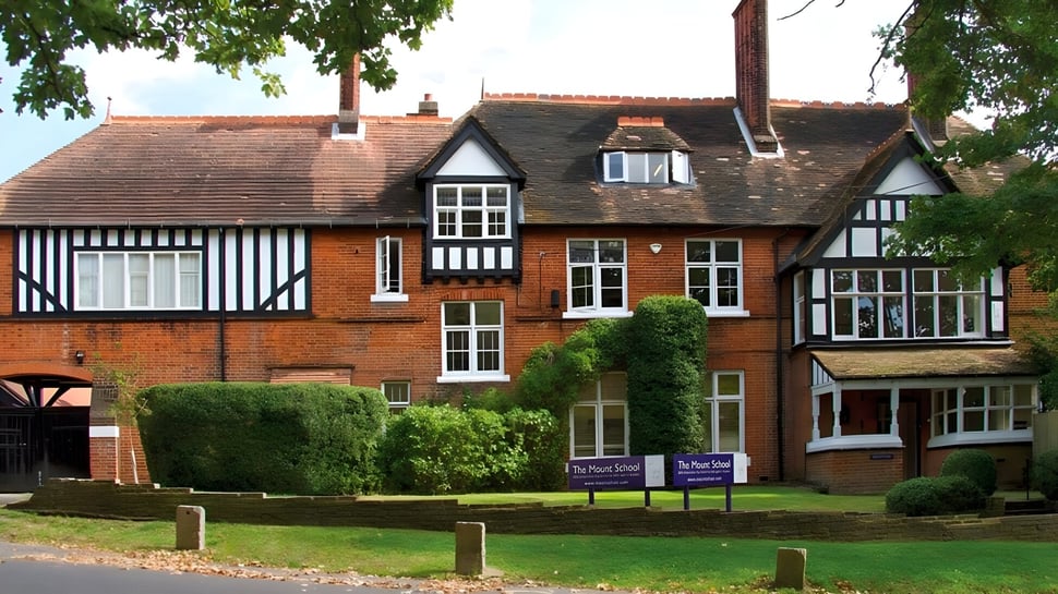 Das Tudor-Stil Gebäude mit Ziegeldach auf dem Campus der Mill Hill International School ist von gepflegtem Rasen und Grünflächen umgeben.