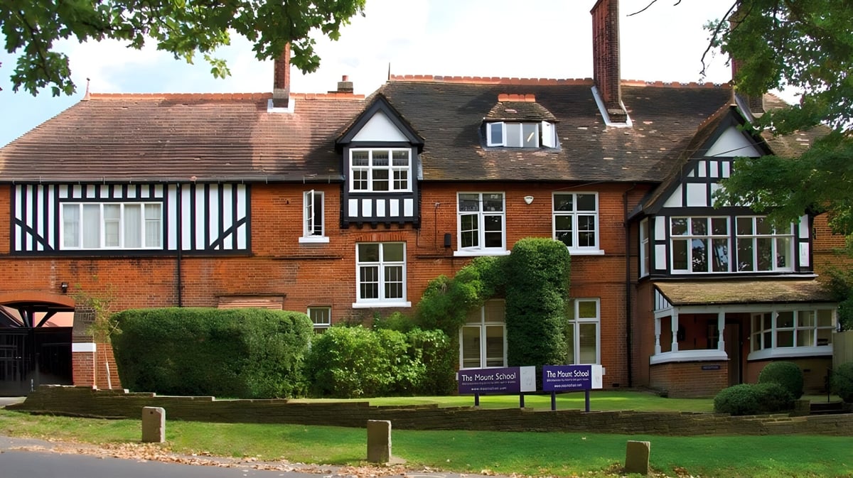 Das Tudor-Stil Gebäude mit Ziegeldach auf dem Campus der Mill Hill International School ist von gepflegtem Rasen und Grünflächen umgeben.