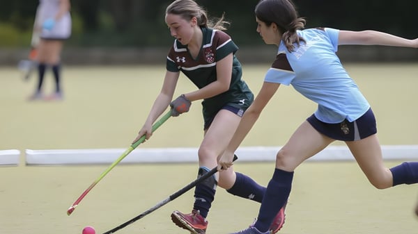 Zwei Sportlerinnen der Mill Hill School spielen ein Hockeyspiel auf einem Grasfeld.