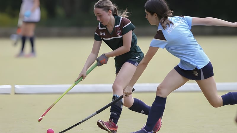 Zwei Sportlerinnen der Mill Hill School spielen ein Hockeyspiel auf einem Grasfeld.