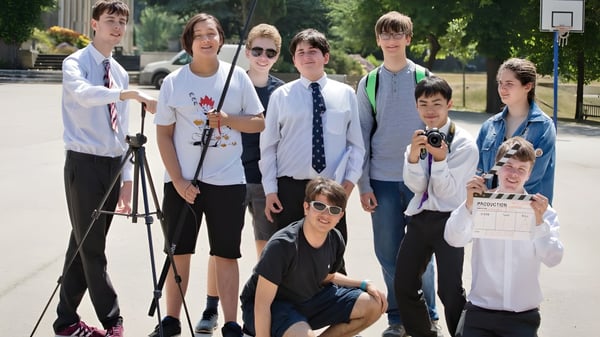 Eine Gruppe Schüler der Mill Hill School steht gemeinsam draußen in der Nähe eines Basketballkorbs.