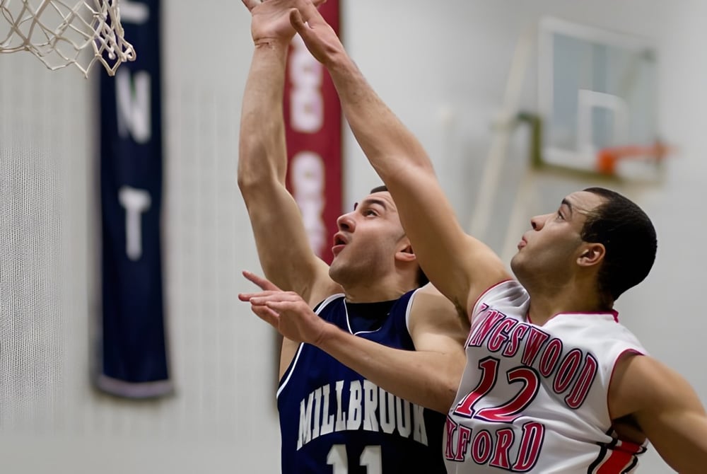 Zwei Schüler der Millbrook School kämpfen um den Ball an einem Basketballkorb in der Turnhalle.