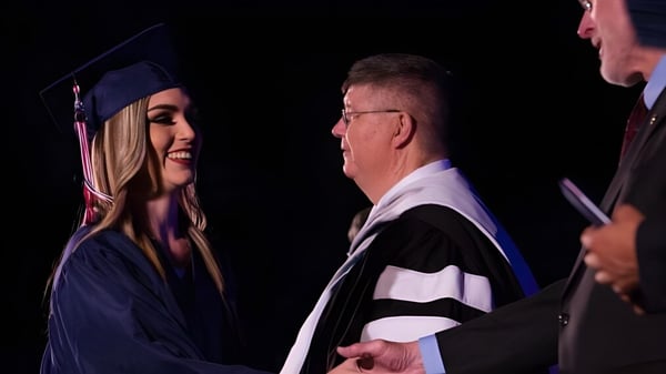 Eine junge Absolventin der Millfield School schüttelt einem älteren Mann in akademischer Robe die Hand während einer Feier.