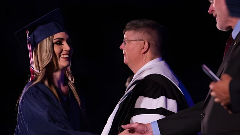 Eine junge Absolventin der Millfield School schüttelt einem älteren Mann in akademischer Robe die Hand während einer Feier.