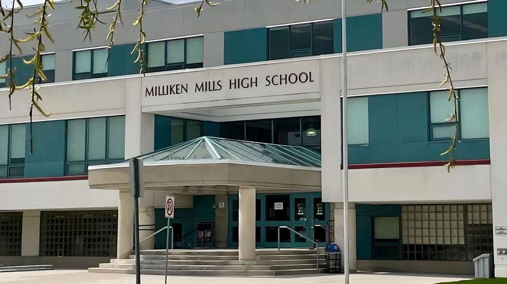 Der Eingang des modernen Gebäudes der Milliken Mills Secondary School ist mit Glas und Beton gestaltet und von hängenden Pflanzen umgeben.
